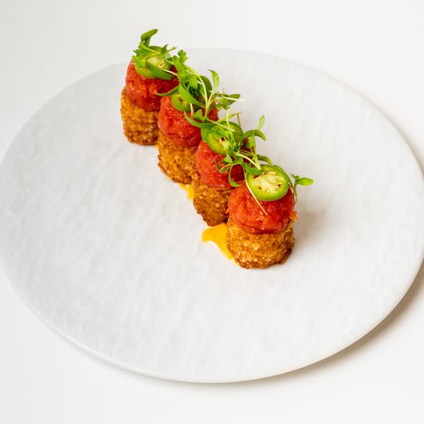 Four crispy rice cakes topped with red tuna tartare, microgreens, and sliced jalapeños on a white plate.