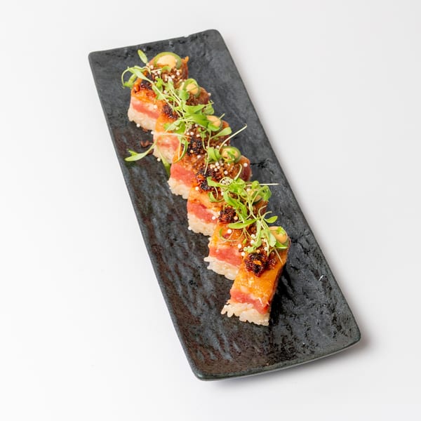 Five pieces of sushi with tuna, rice, microgreens, and sauce on a black rectangular plate.