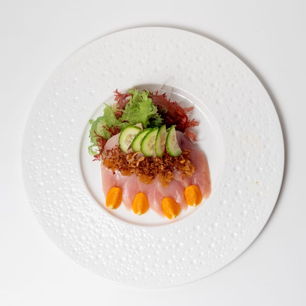 Sashimi dish with sliced fish, seaweed, cucumbers, fried garlic, and kumquats on a white plate.