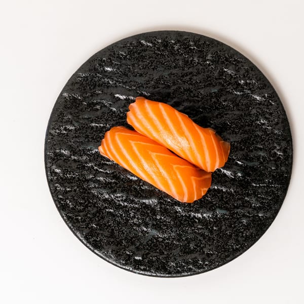 Two pieces of salmon nigiri sushi with vibrant orange fish on a dark textured plate.
