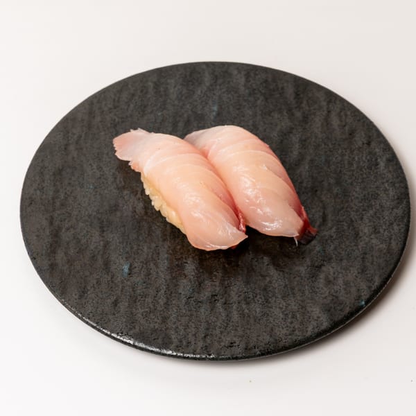 Two pieces of light pink nigiri sushi with white rice on a dark, textured plate.