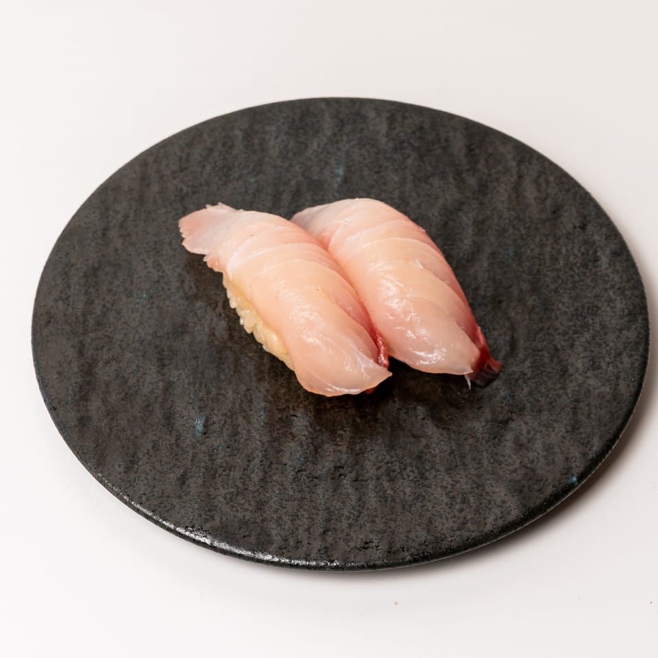 Two pieces of light pink nigiri sushi with white rice on a dark, textured plate.