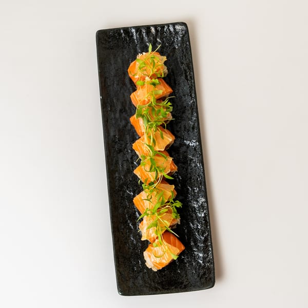 Salmon sushi rolls with microgreens on a rectangular black plate.