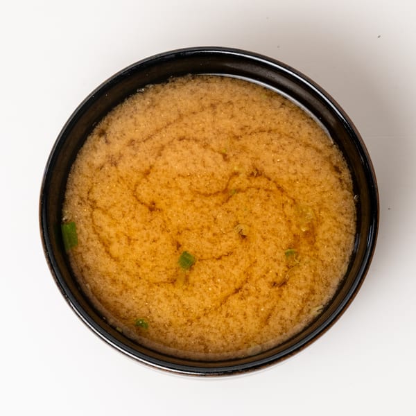 Overhead view of a dark bowl filled with miso soup, garnished with green onions.