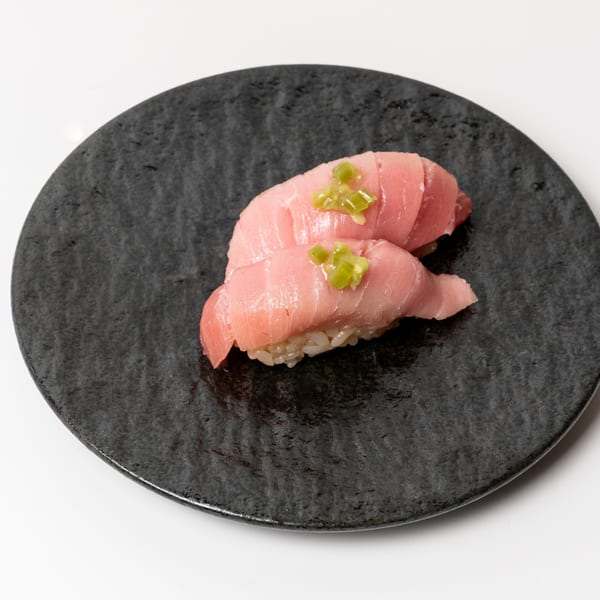 Two pieces of pink tuna nigiri sushi with green garnish on a dark textured plate.