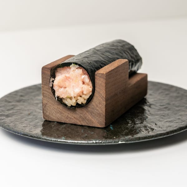 A hand roll sushi with minced salmon and rice, served in a wooden holder on a dark plate.