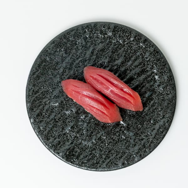 Two pieces of red tuna nigiri sushi with scored tops, presented on a dark textured plate.