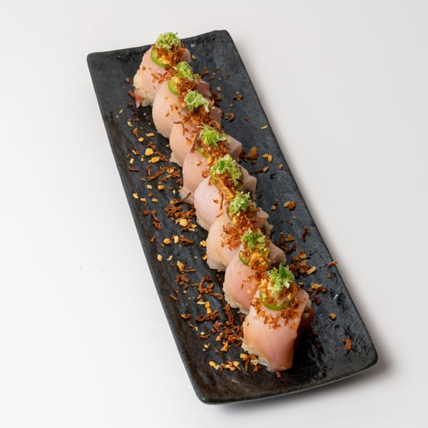 Seven pieces of sushi with seared fish, green onions, and crispy fried garlic on a black plate.
