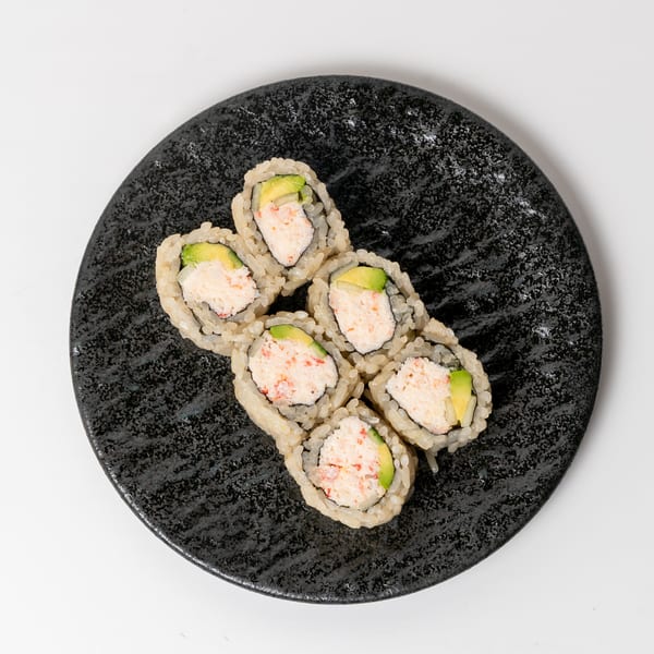 Six California rolls with crab and avocado on a textured black plate.