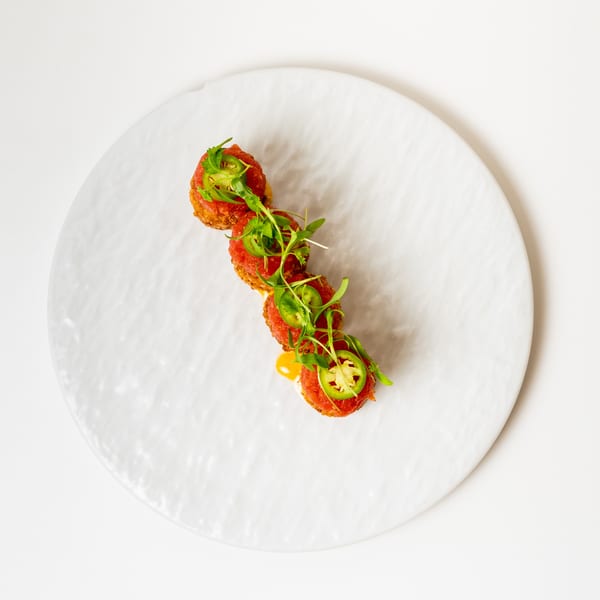 Four crispy tuna tartare bites topped with microgreens and jalapeño slices on a white plate.
