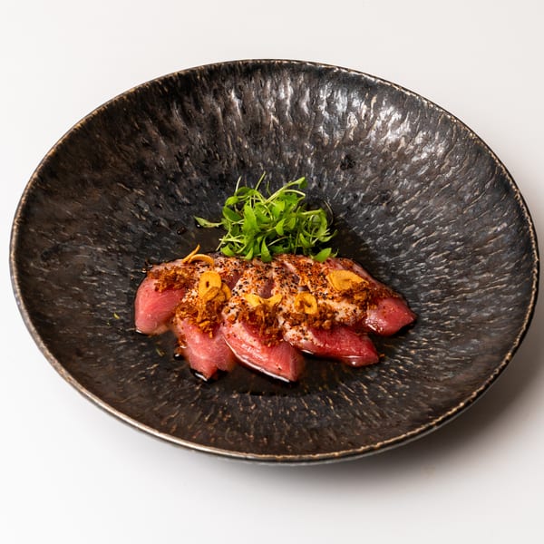Seared tuna sashimi with microgreens, crispy garlic, and spices in a dark, textured bowl.
