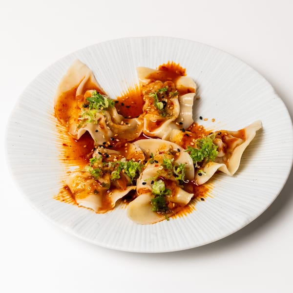 A plate of dumplings drizzled with chili oil, sesame seeds, and chopped green onions.