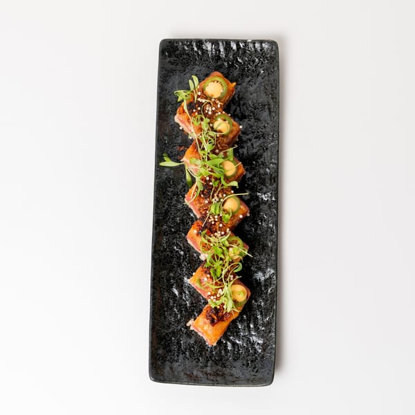 Seared tuna sushi rolls with jalapeño, microgreens, and sauce on a black rectangular plate.