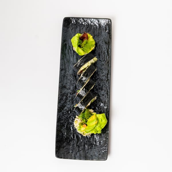Sushi rolls with avocado and lettuce on a black rectangular plate.